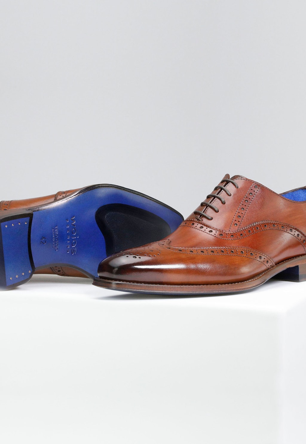 Eleganckie oxfordy męskie Wojas PREMIUM 10061-52 w jasnobrązowym kolorze z charakterystyczną brogue perforacją i niebieską podeszwą, ukazane z boku i od spodu.