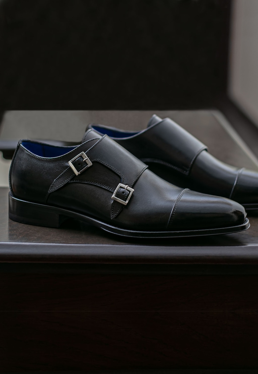 Eleganckie czarne monki Wojas PREMIUM model 10059-51 z dwiema metalowymi klamrami, widoczne z boku na metalowej powierzchni, wykonane z wysokiej jakości skóry.