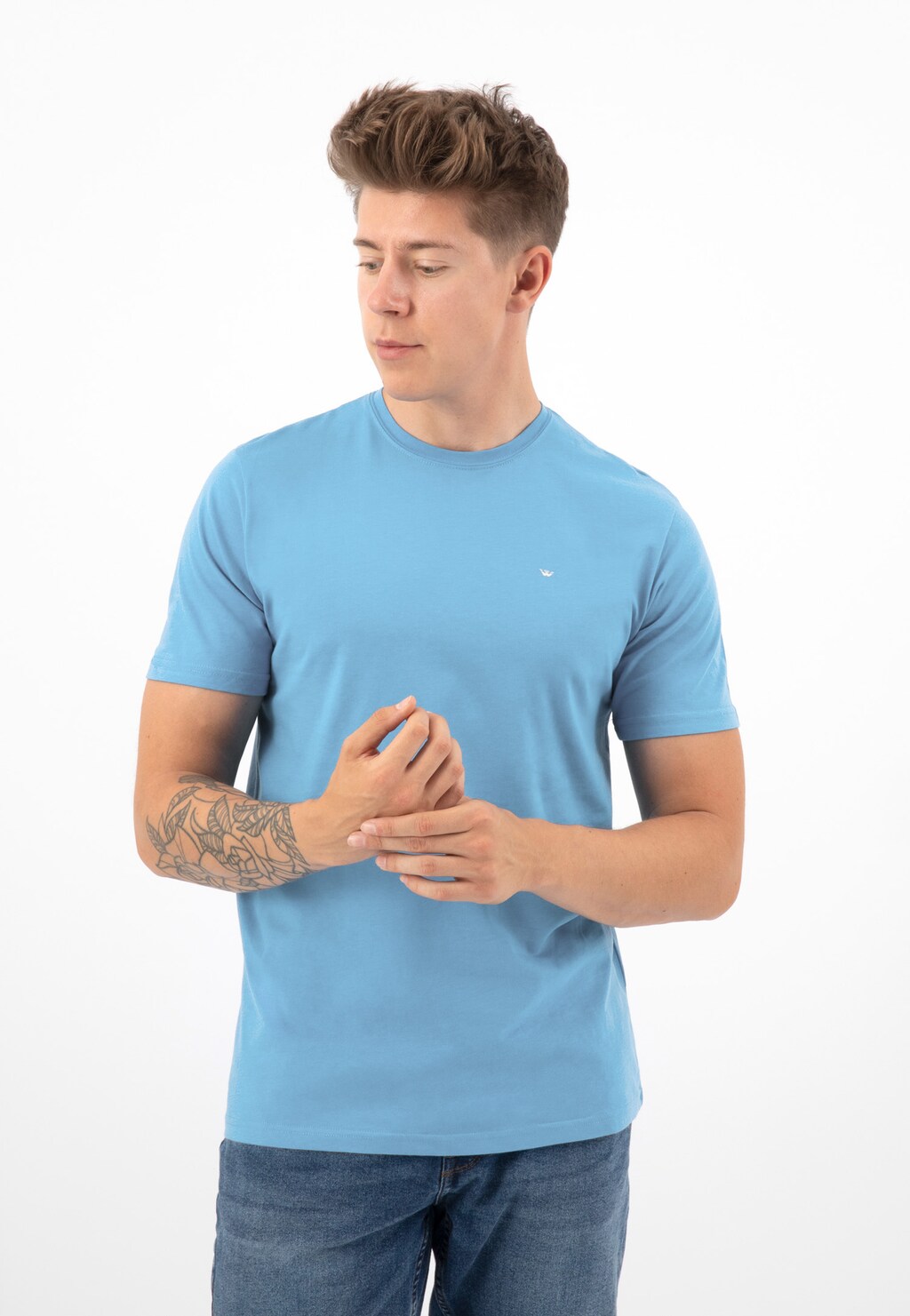 Jasnoniebieski t-shirt męski Wojas 98018-88 prezentowany na modelu w dżinsach. Klasyczny krój z okrągłym dekoltem, widoczny tatuaż na przedramieniu.