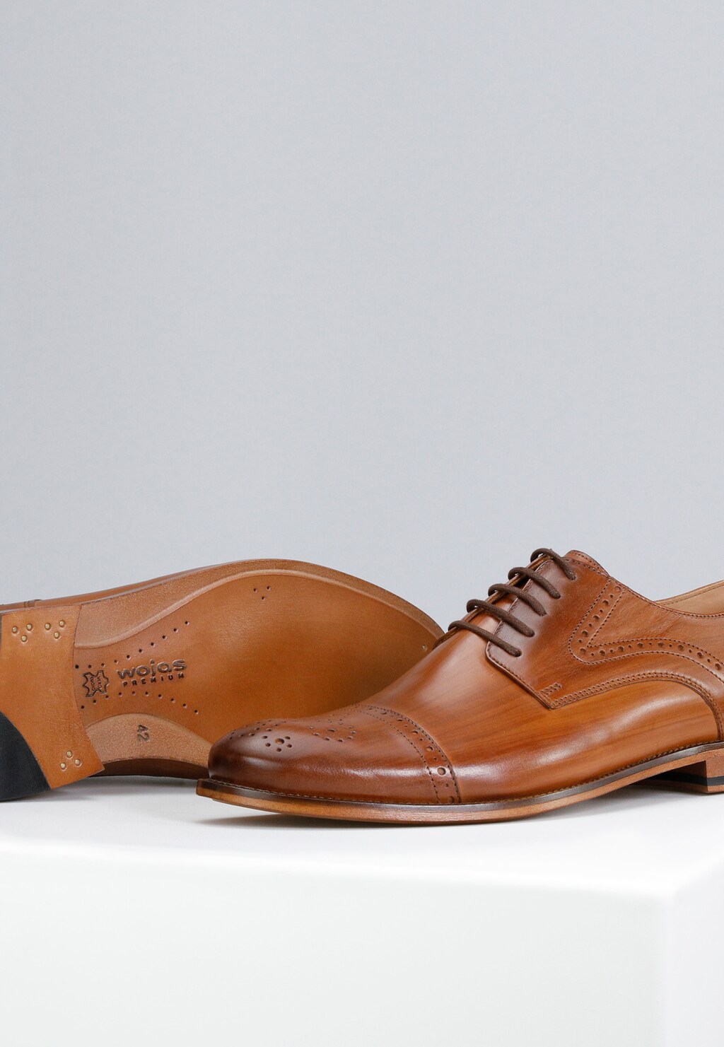Jasnobrązowe wizytowe półbuty męskie Wojas PREMIUM model 10054-53 z ozdobną perforacją, widok z boku oraz podeszwy z logo marki, wykonane z wysokiej jakości skóry.