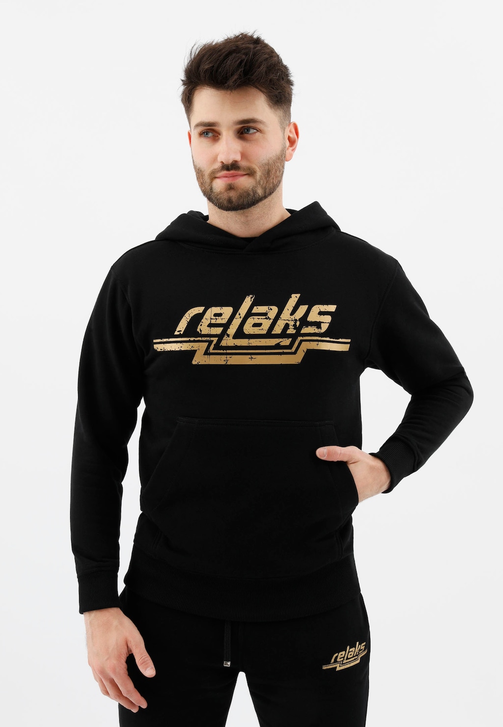 Czarna bluza męska RELAKS model 98020-81 z kapturem i złotym logo na przodzie, z kieszenią kangurką, prezentowana na modelu w komplecie ze spodniami tej samej marki.
