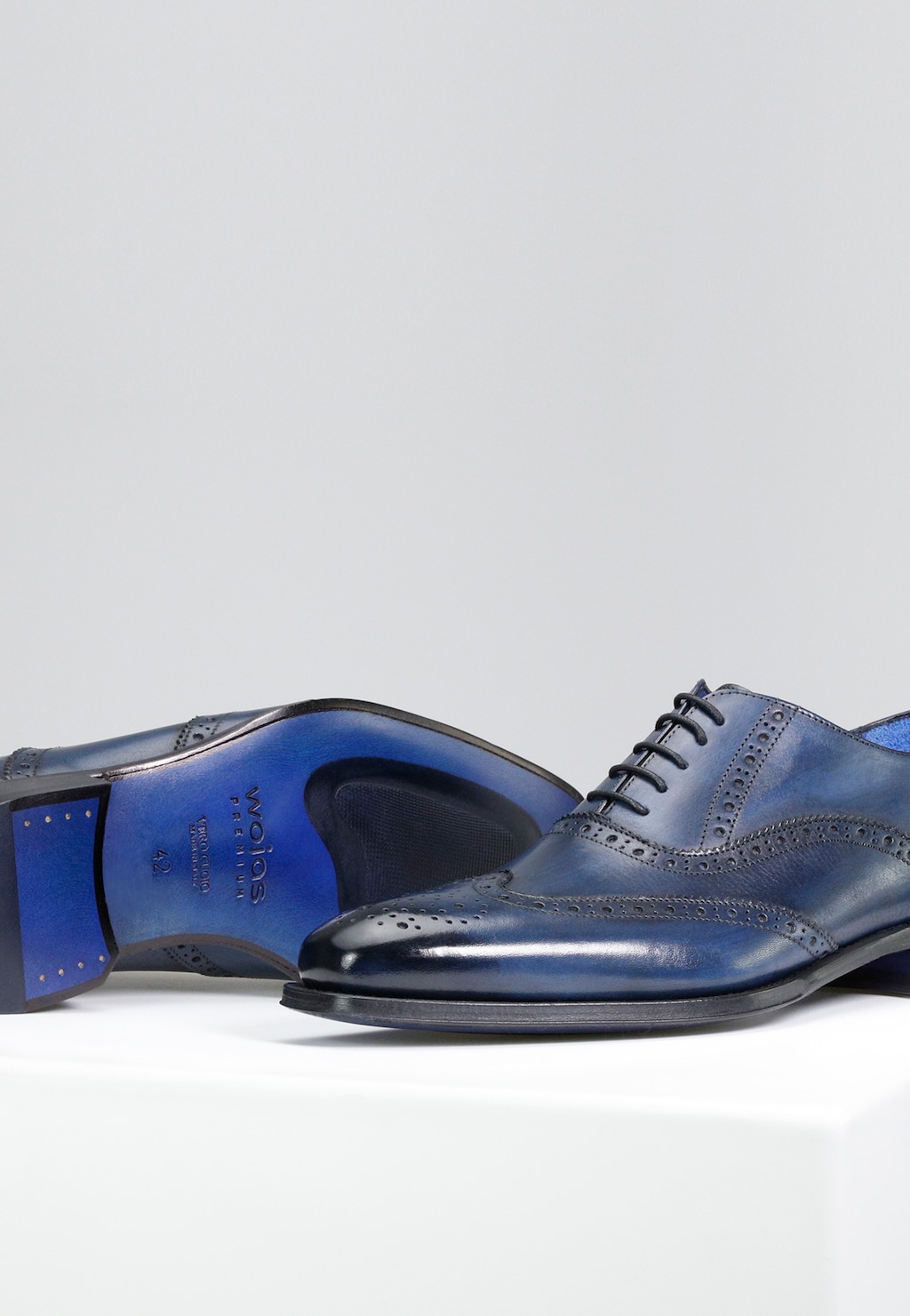 Eleganckie granatowe półbuty męskie Wojas PREMIUM model 10060-56 w stylu oxford z charakterystyczną perforacją brogues, widoczną niebieską podeszwą i logiem marki.