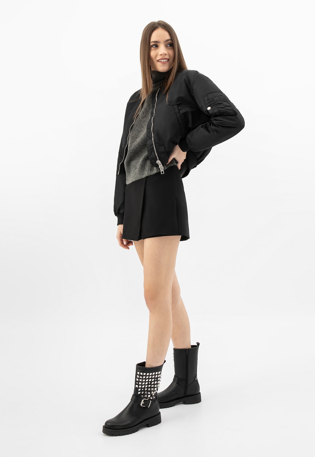 Modelka w modnej stylizacji prezentuje czarne skórzane bikery Wojas 55250-51 z charakterystycznymi ćwiekami na cholewce, noszone ze spódnicą, czarną bomberką i szarym swetrem.