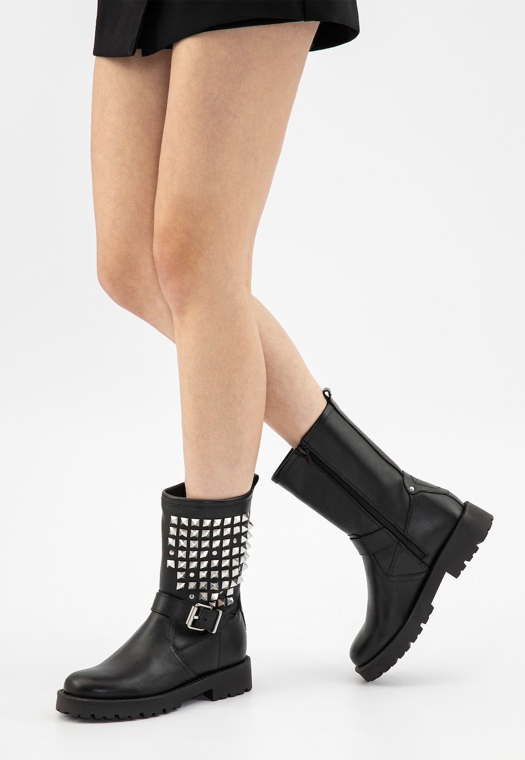 Czarne skórzane bikery damskie Wojas 55250-51 z ozdobnymi srebrystymi ćwiekami na cholewce i klamrą, na grubej podeszwie, prezentowane na nogach modelki w krótkiej spódnicy.