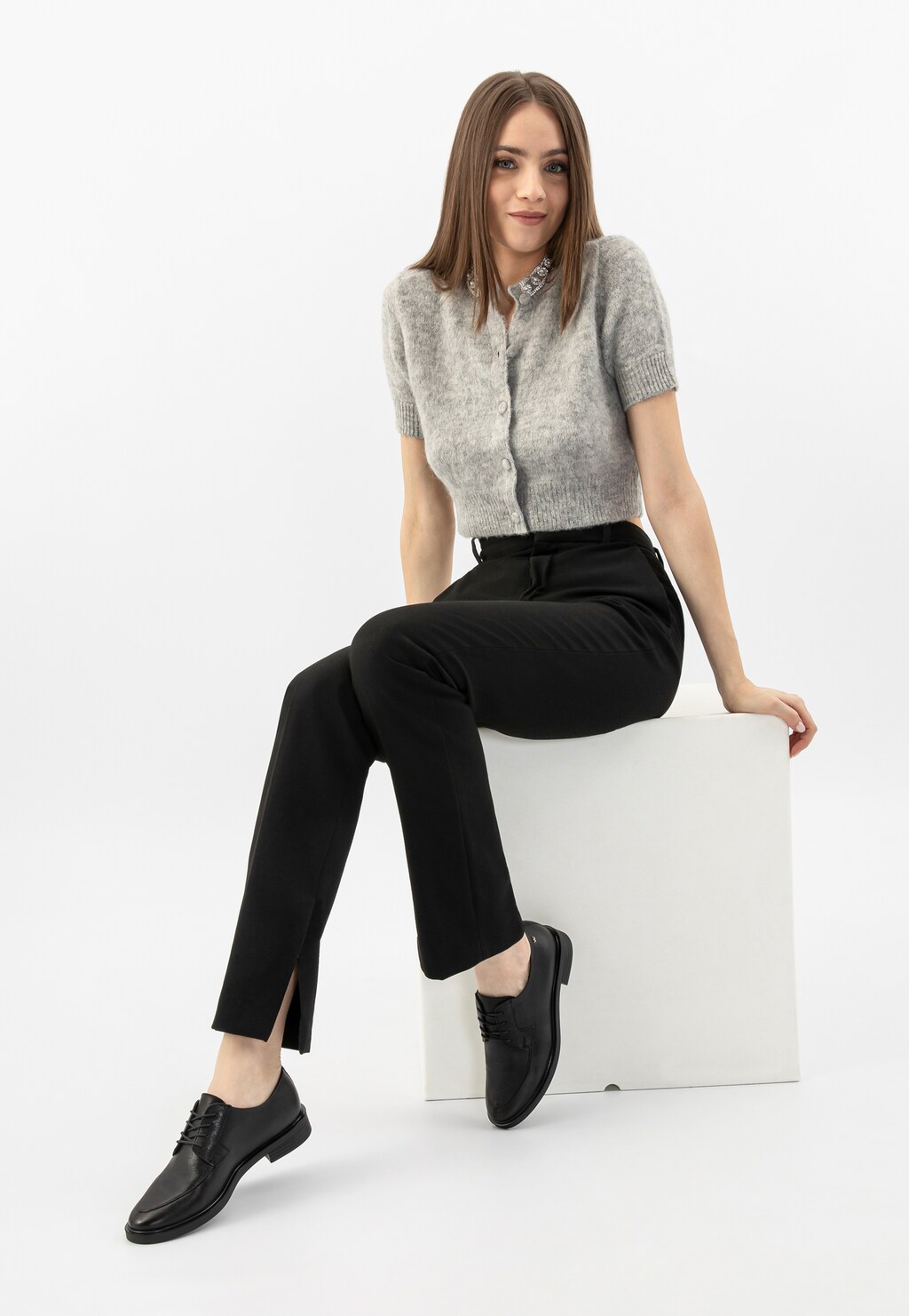 Modelka w szarym sweterku i czarnych spodniach prezentuje czarne eleganckie półbuty damskie sznurowane Wojas model 46250-51 w stylizacji biznesowej.