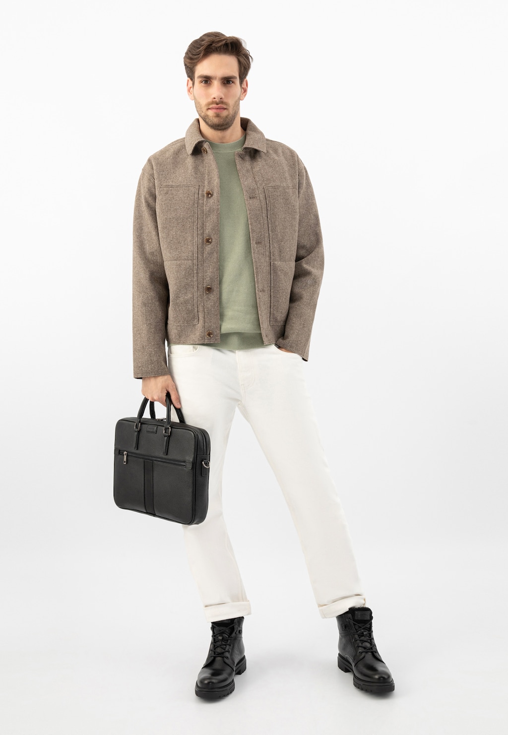 Model prezentuje czarną skórzaną torbę męską Wojas 90014-51 z kieszonką na zamek. Stylizacja z beżową kurtką, zieloną koszulką i białymi spodniami podkreśla elegancki charakter torby.