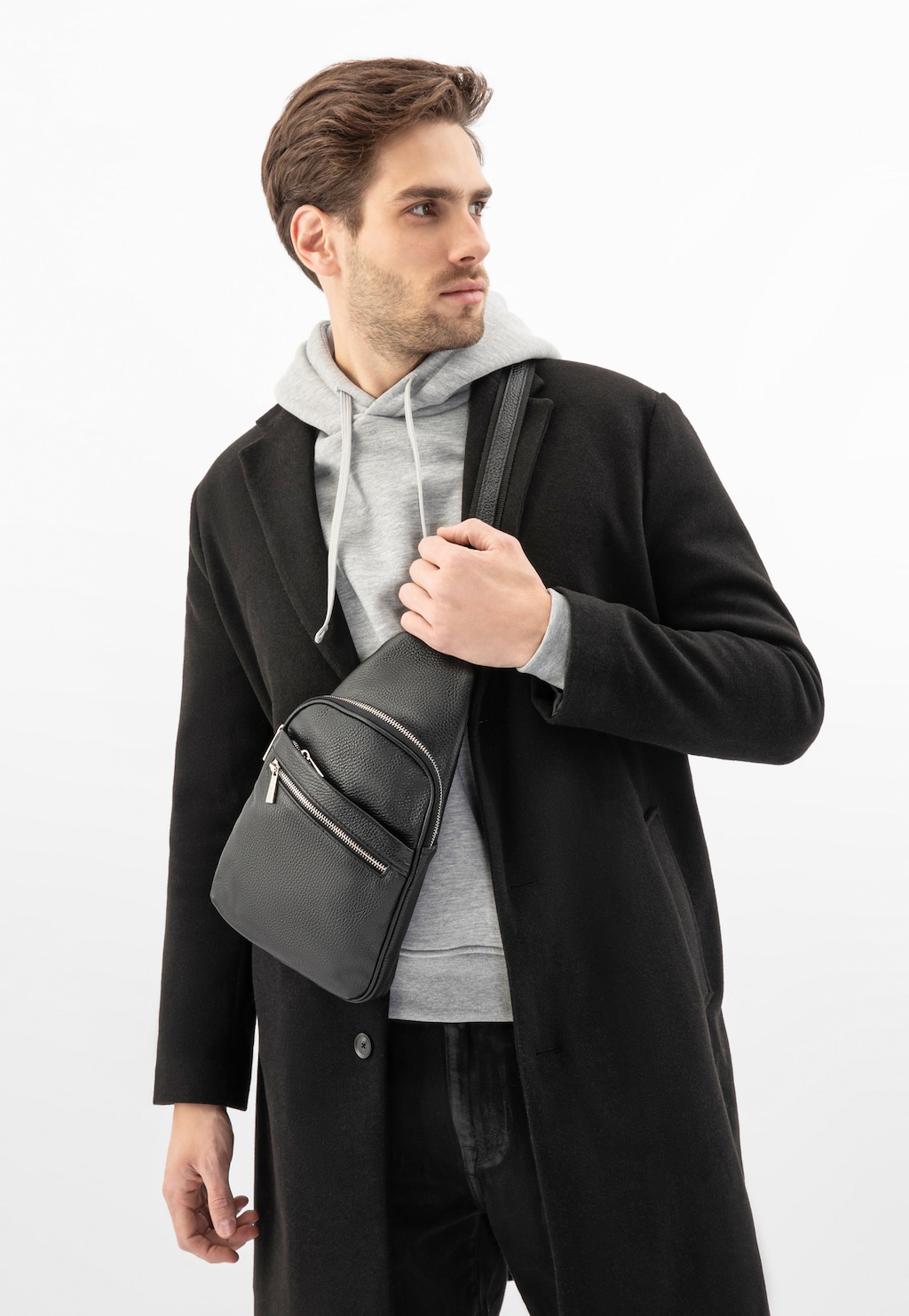 Elegancka czarna torba męska Wojas 80193-51 ze skóry licowej z przednią kieszenią zapinaną na zamek, prezentowana na modelu w czarnym płaszczu i szarej bluzie z kapturem.