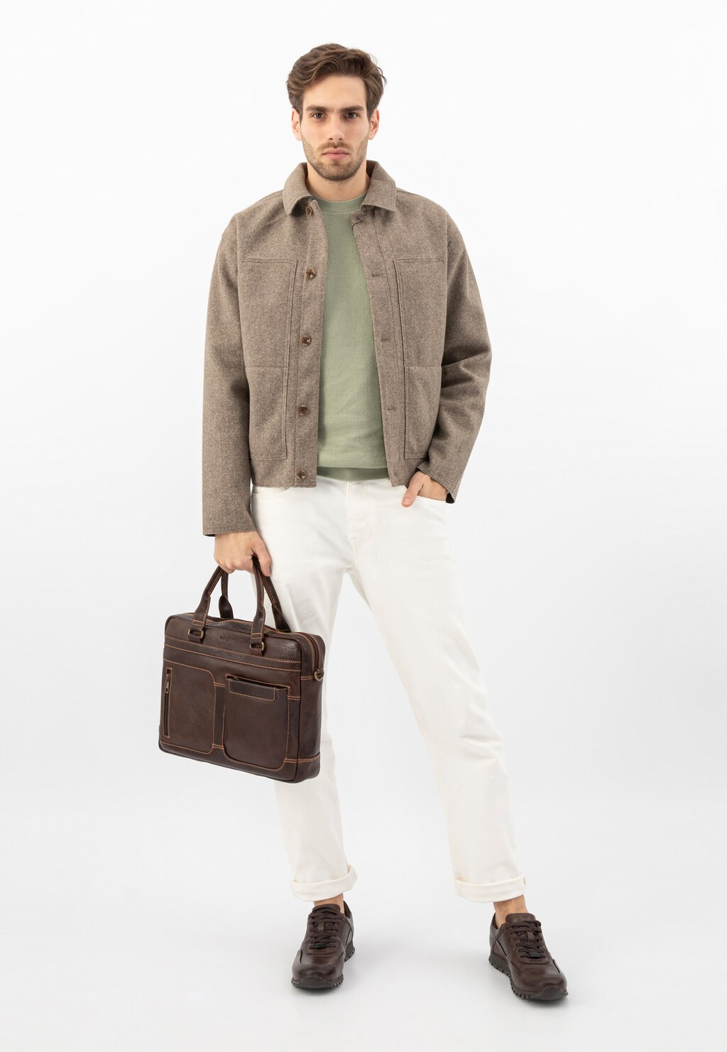 Model prezentujący brązową skórzaną torbę męską Wojas 80141-52 do pracy, ubrany w beżową kurtkę, zieloną koszulkę i białe spodnie, z brązowymi butami.