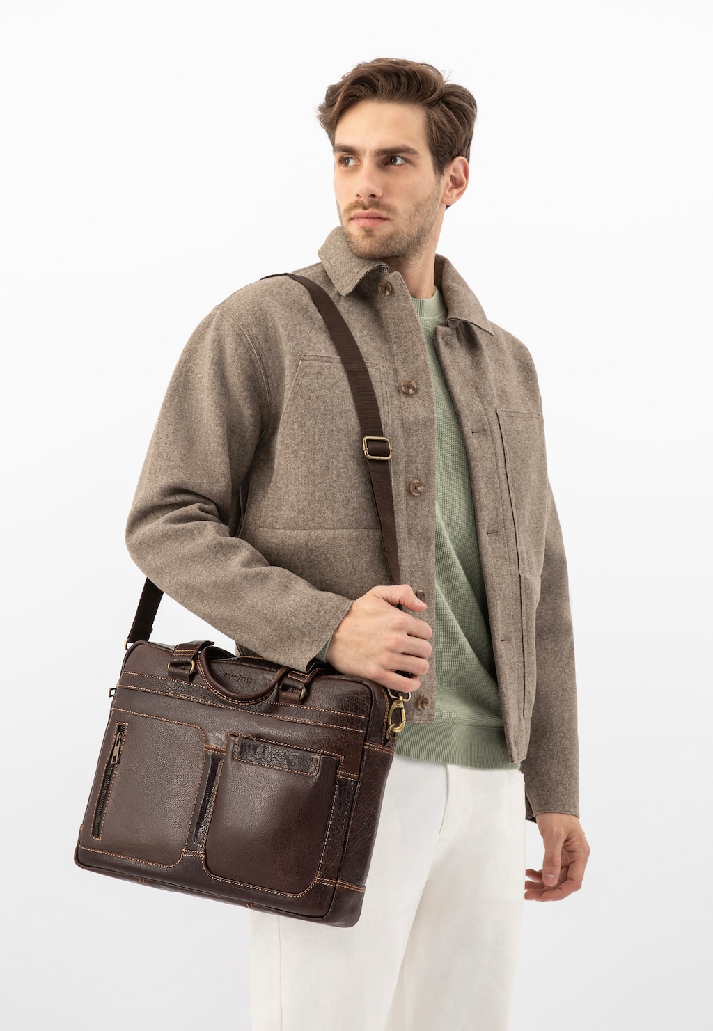 Brązowa skórzana torba męska Wojas 80141-52 prezentowana na ramieniu osoby w beżowej marynarce i zielonym swetrze. Widoczne kieszenie i paski torby biznesowej.