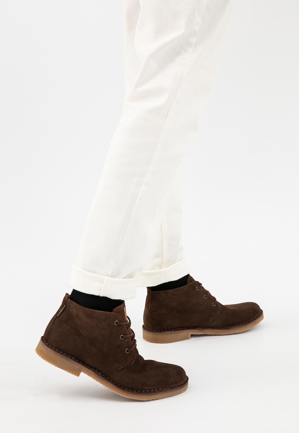 Brązowe trzewiki męskie Wojas model 24400-63 typu desert boots wykonane z dwoiny welurowej, noszone z białymi spodniami, widok z boku na nogi.