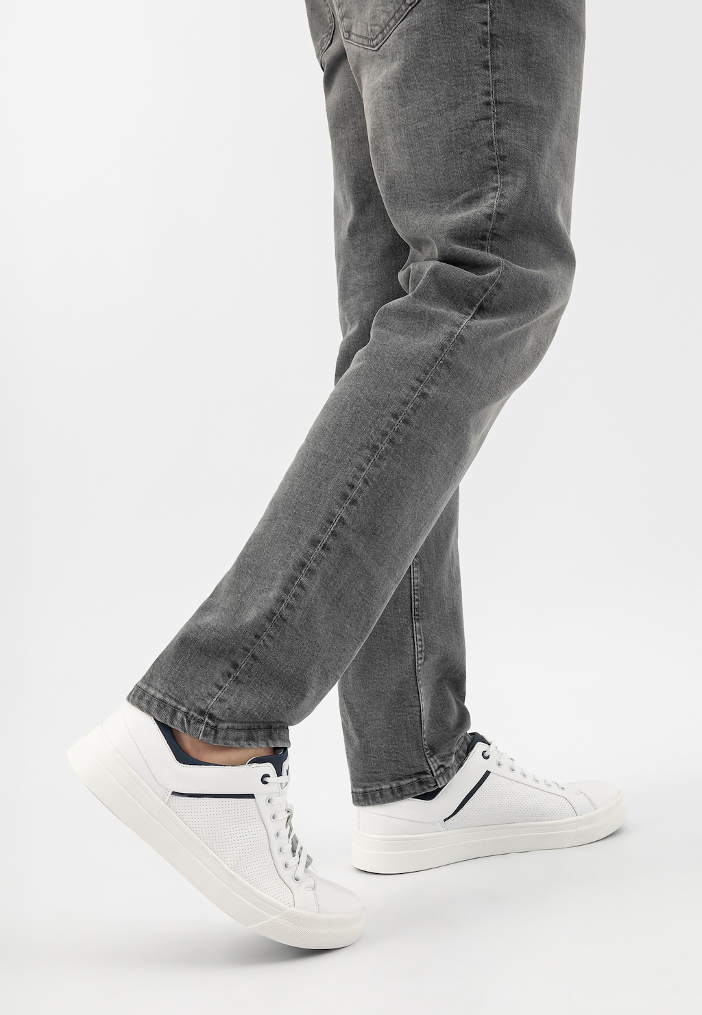 Białe trampki męskie Wojas model 10199-50 z granatowymi wstawkami na stopach osoby w szarych jeansach. Widok z boku, ukazujący perforowaną skórę i biały design.