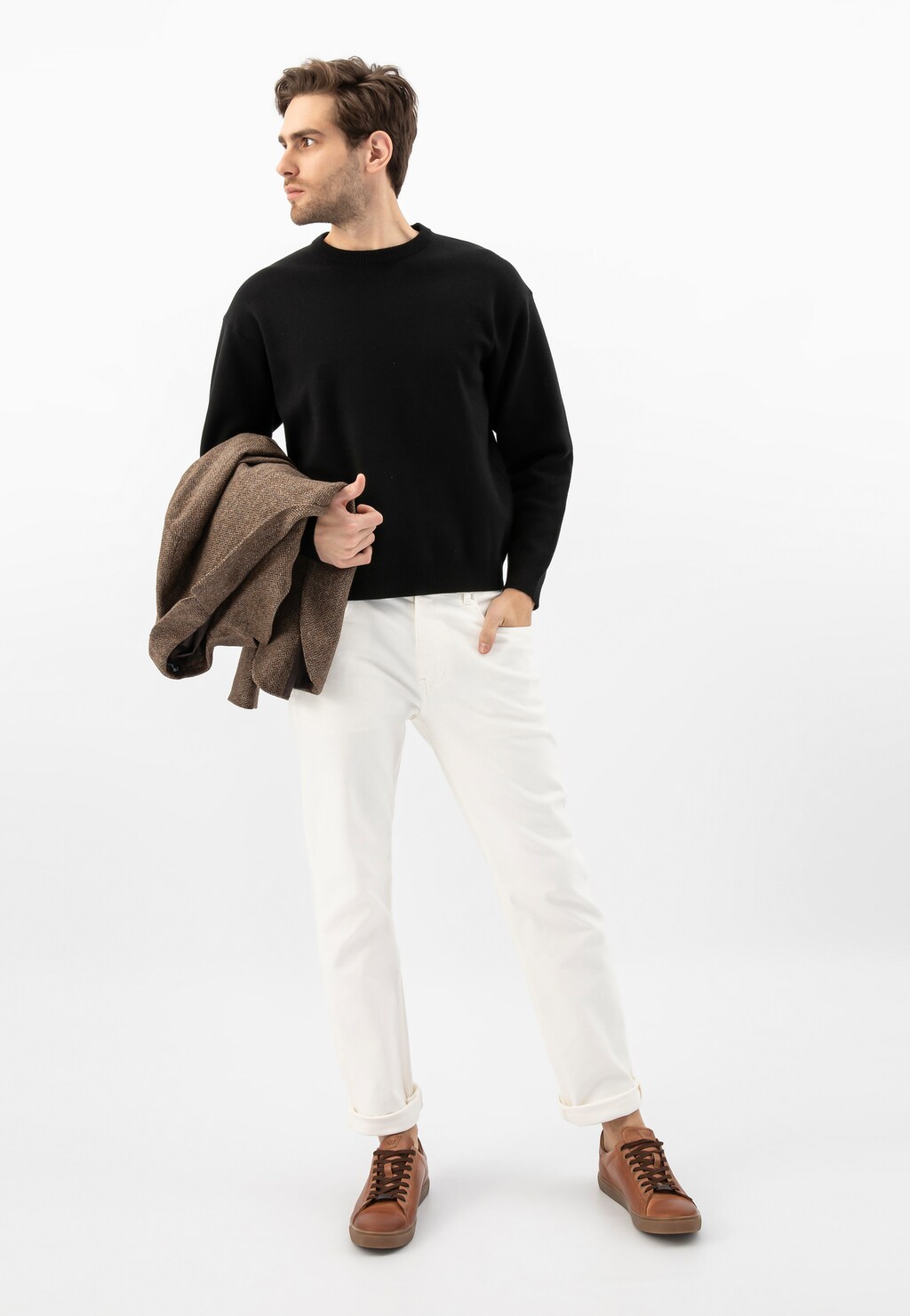 Model w czarnym swetrze i białych spodniach, prezentujący jasnobrązowe trampki Wojas ze skóry licowej, model 10170-53, trzymający w ręku brązową marynarkę.