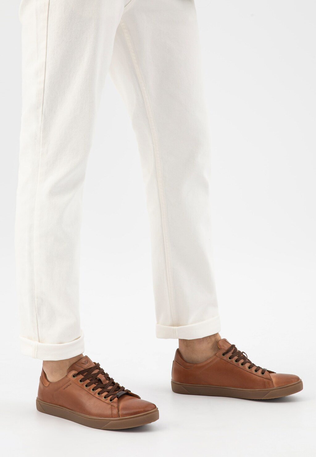 Jasnobrązowe trampki męskie Wojas 10170-53 ze skóry licowej z brązową podeszwą, prezentowane na nogach osoby w białych spodniach, widok z boku.