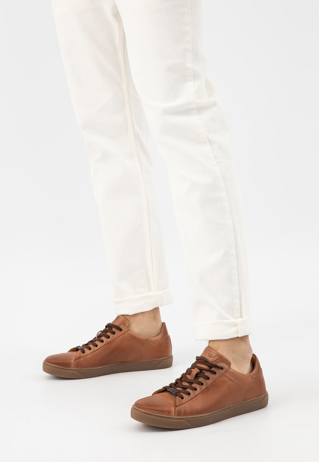 Jasnobrązowe trampki męskie Wojas 10170-53 ze skóry licowej na gumowej podeszwie, noszone z białymi spodniami. Pokazane z boku w ujęciu od kolan w dół.