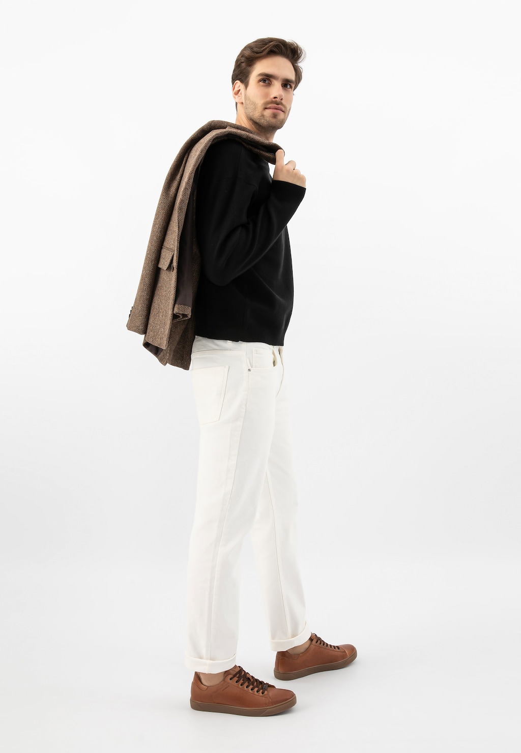 Stylizacja z jasnobrązowymi trampkami Wojas 10170-53 ze skóry licowej, białymi spodniami i czarnym swetrem. Mężczyzna niesie brązowy płaszcz na ramieniu.