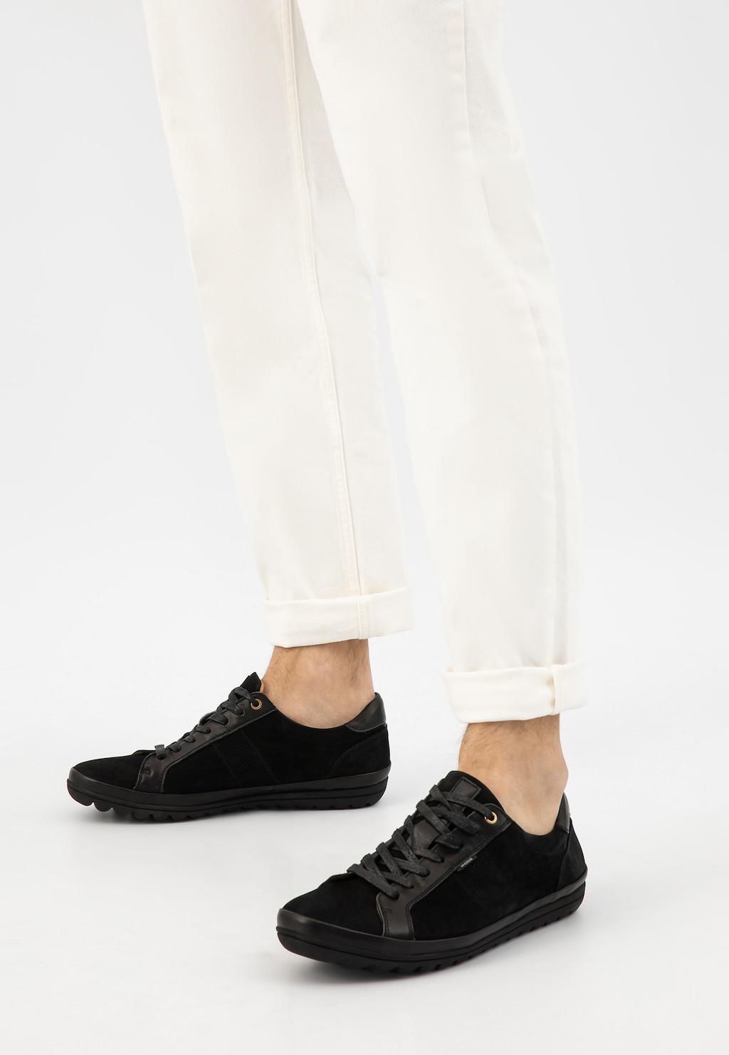 Czarne męskie sneakersy Wojas model 10147-71 na nogach osoby w białych spodniach, widok z boku. Buty z oryginalną podeszwą i zamszowym wykończeniem.