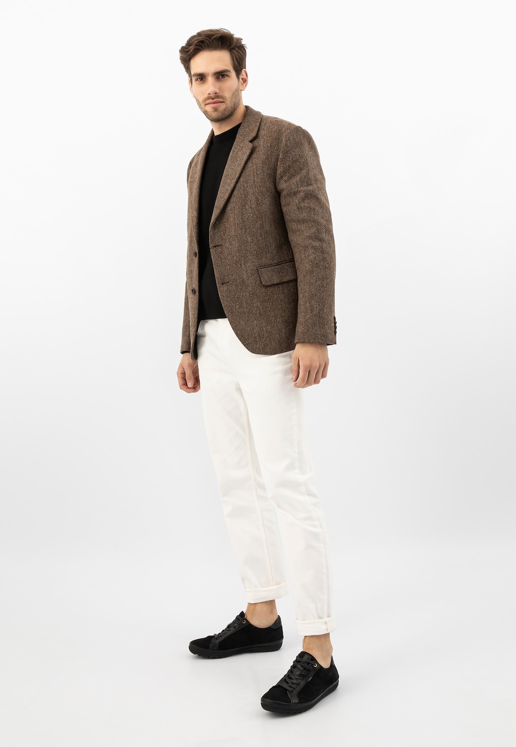 Model ubrany w elegancki brązowy płaszcz, czarny t-shirt i białe spodnie, prezentujący czarne męskie sneakersy Wojas model 10147-71 na oryginalnej podeszwie.