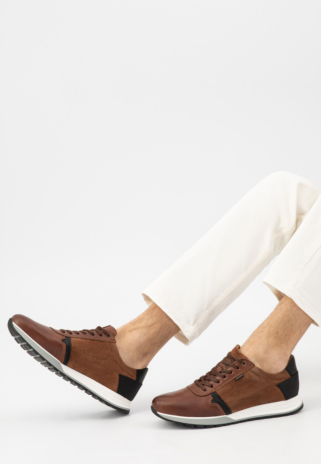 Jasnobrązowe sneakersy męskie Wojas 10021-73 z czarnymi akcentami na pięcie i bokach, noszone z białymi spodniami, widok z boku ukazujący sportowy profil obuwia.