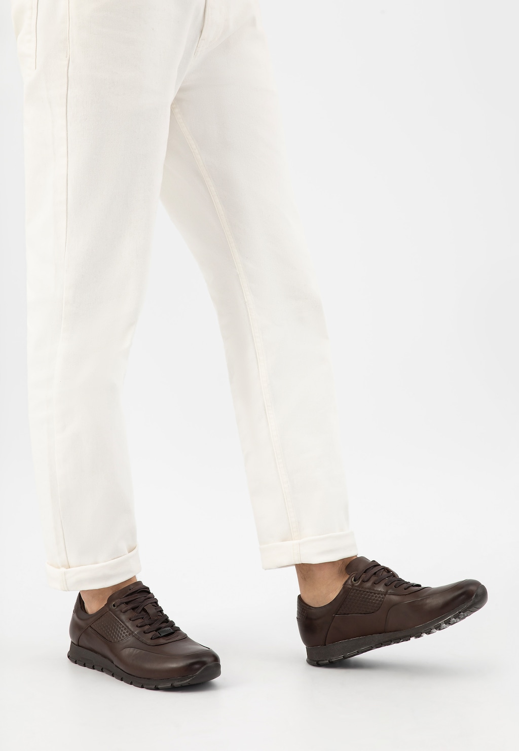 Ciemnobrązowe sneakersy męskie Wojas model 9078-52 ze skóry licowej na stopach osoby ubranej w białe spodnie, widok z boku pokazujący perforowany wzór na cholewce.