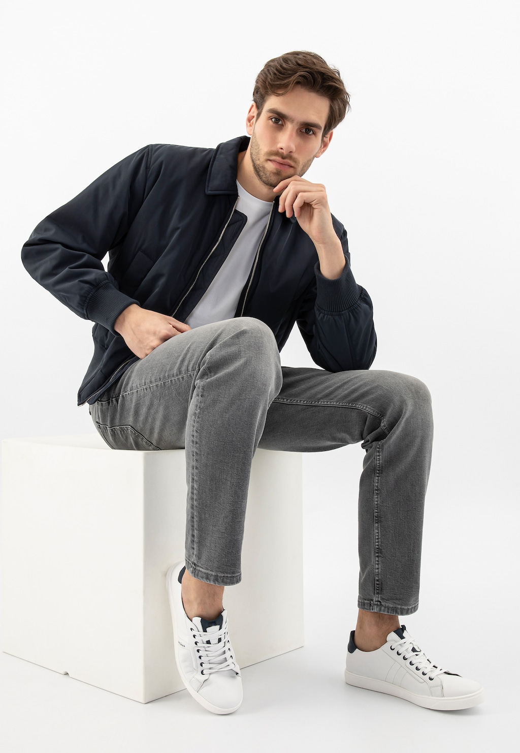 Osoba w modnej stylizacji z czarną kurtką i szarymi dżinsami, prezentująca białe skórzane półbuty męskie Wojas model 10167-57 z granatowymi wstawkami.