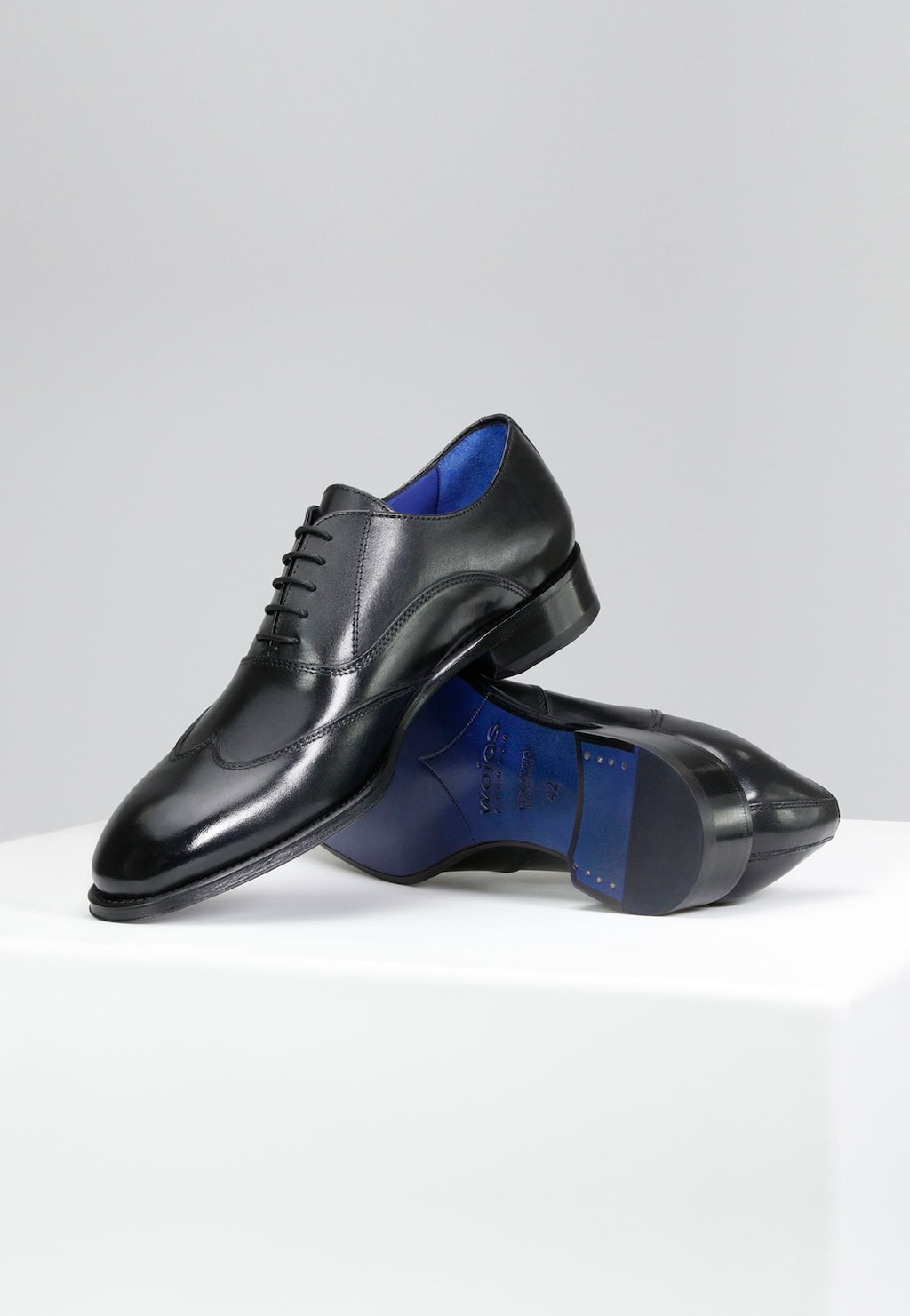 Eleganckie czarne półbuty Wojas PREMIUM 10058-51 z lśniącej skóry, widoczne z boku i od podeszwy, z charakterystycznym niebieskim wykończeniem wnętrza i skórzaną podeszwą.