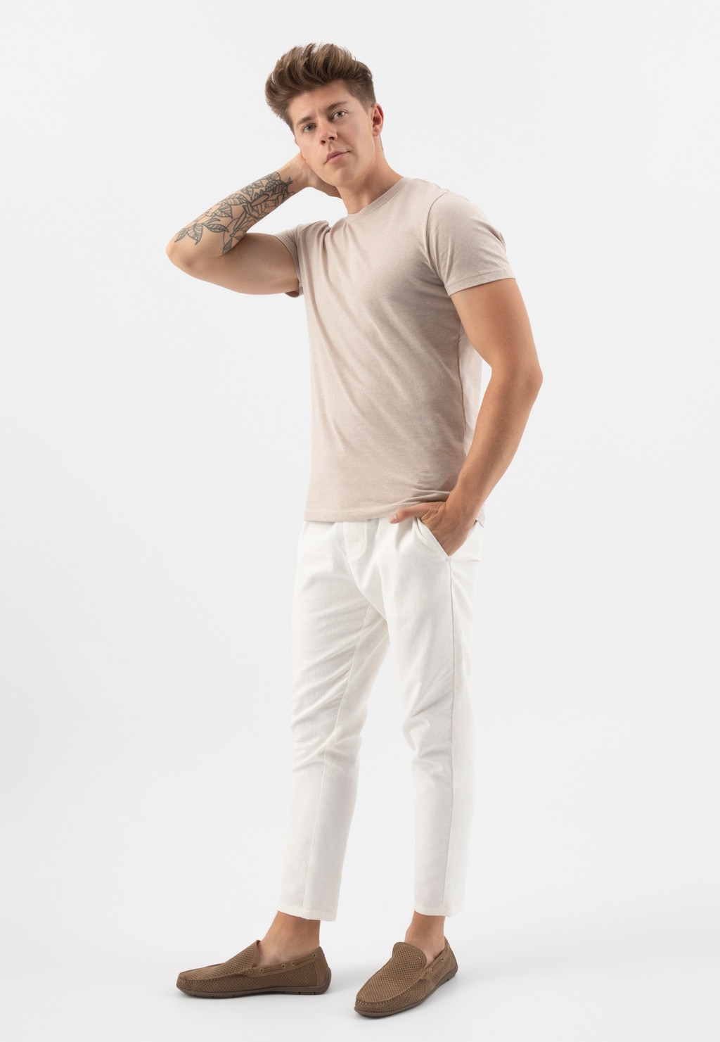 Model w beżowej koszulce i białych spodniach prezentuje beżowe mokasyny męskie Wojas 10103-24 z perforowaną skórą, ukazując ich elegancki i casualowy styl.