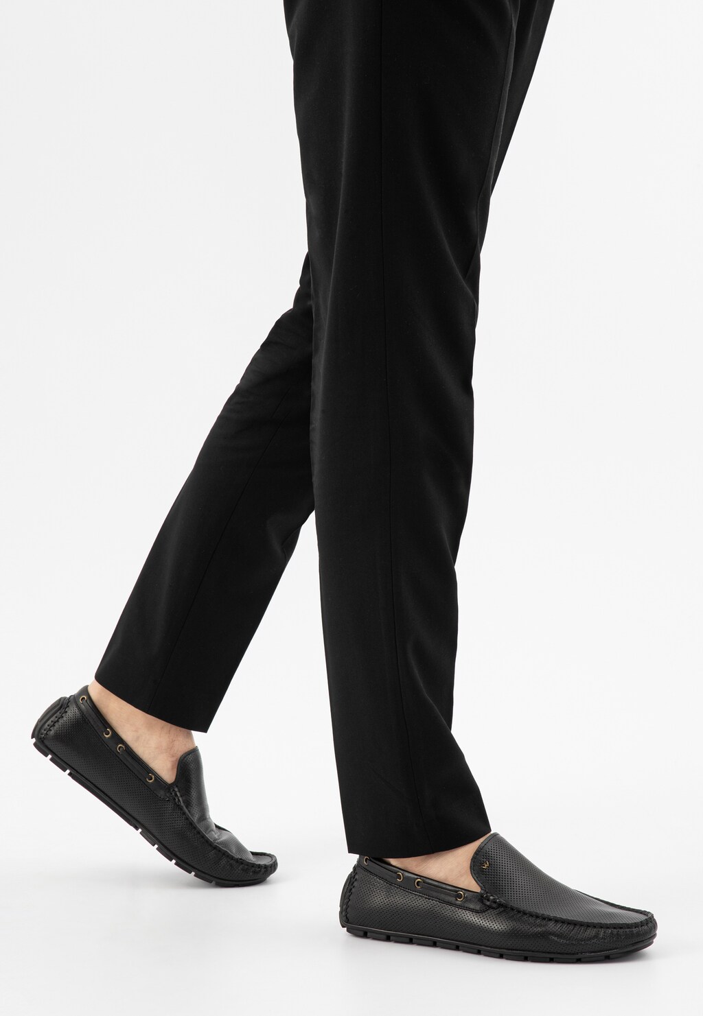 Czarne mokasyny męskie Wojas 10047-51 na stopach modela w czarnych spodniach. Eleganckie buty wiosenne z perforowaną skórą i delikatnymi przeszyciami, idealne do stylizacji biznesowych.