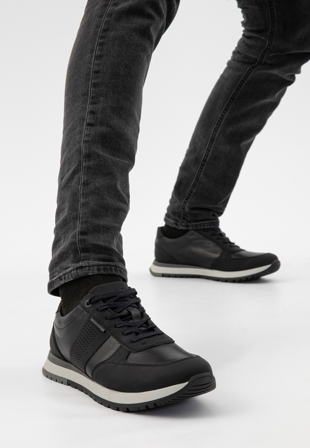 Czarne sneakersy męskie Wojas model 10132-71 noszone z ciemnymi jeansami. Buty z charakterystycznymi szarymi elementami na podeszwie widoczne podczas chodzenia.