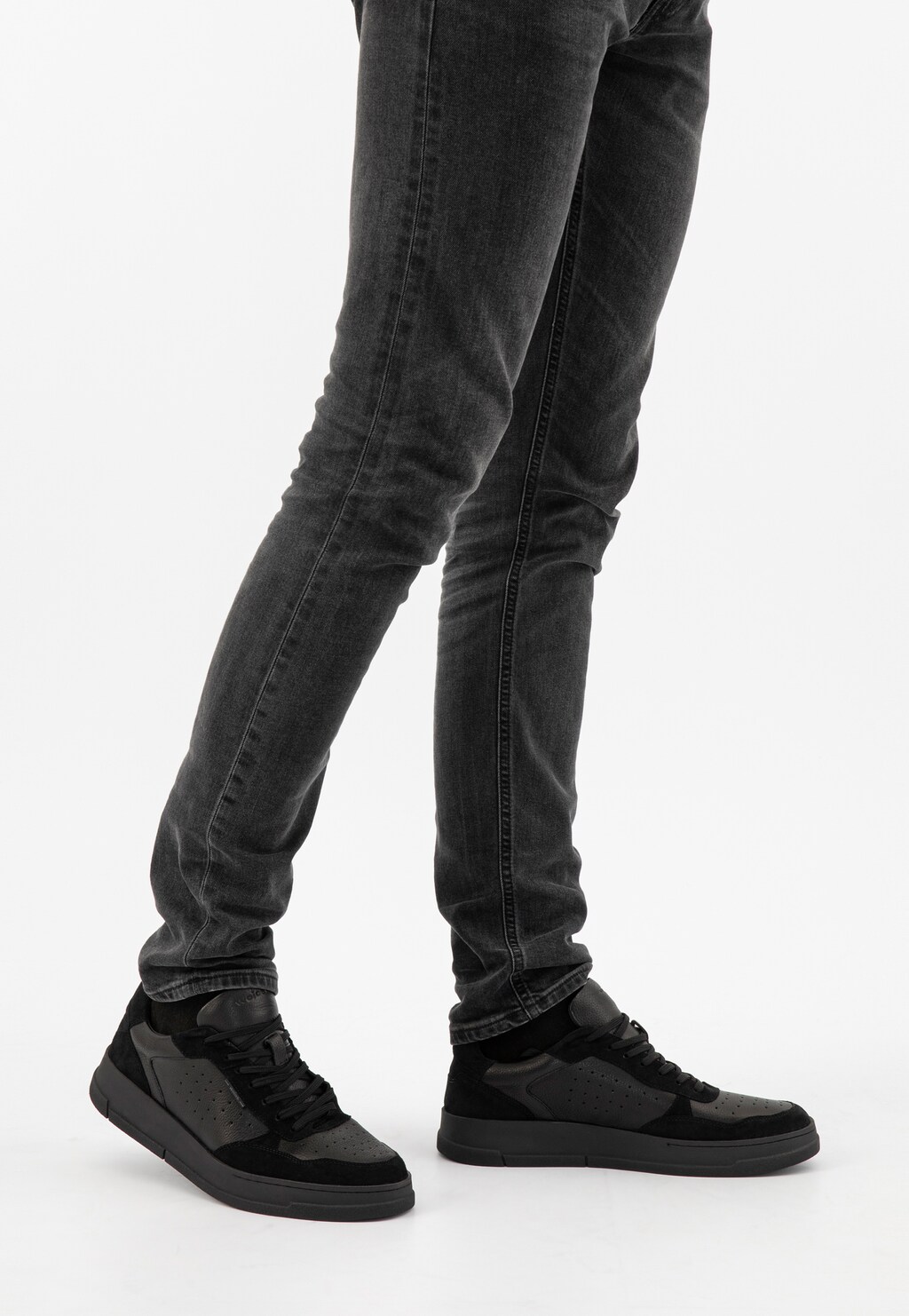 Czarne trampki męskie Wojas model 10141-71 z łączonych skór, widoczne na nogach w szarych jeansach. Sportowe buty o casualowym charakterze z perforacją na cholewce.