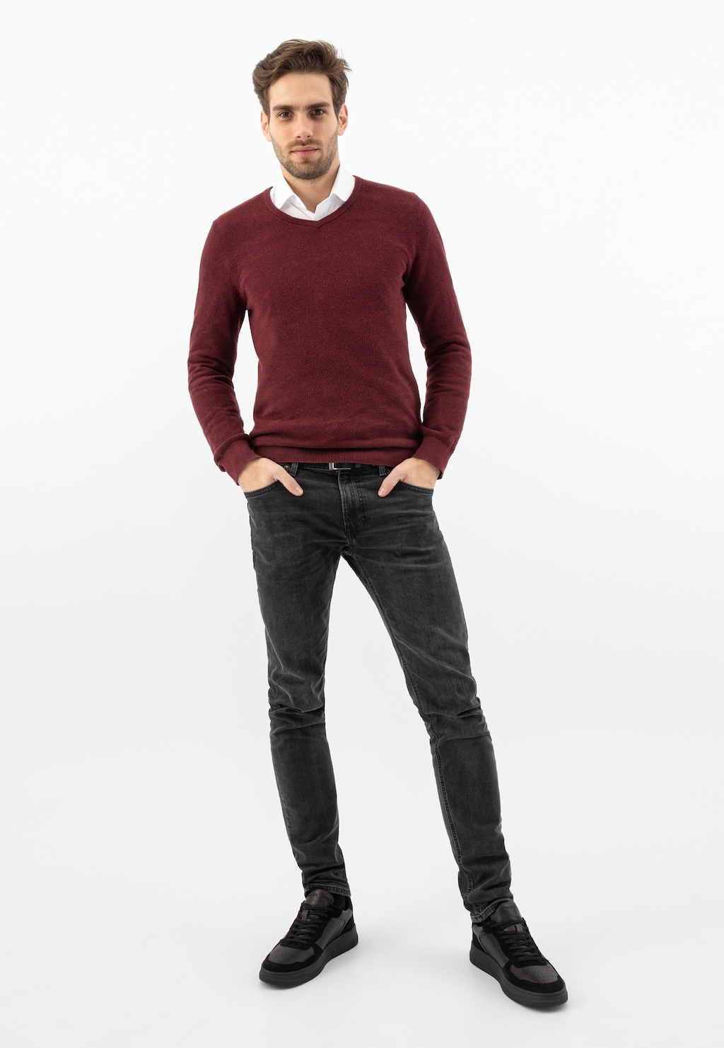 Model w bordowym swetrze i czarnych jeansach prezentuje czarne trampki męskie Wojas model 10141-71 wykonane z łączonych skór, idealnie dopełniające casualową stylizację.