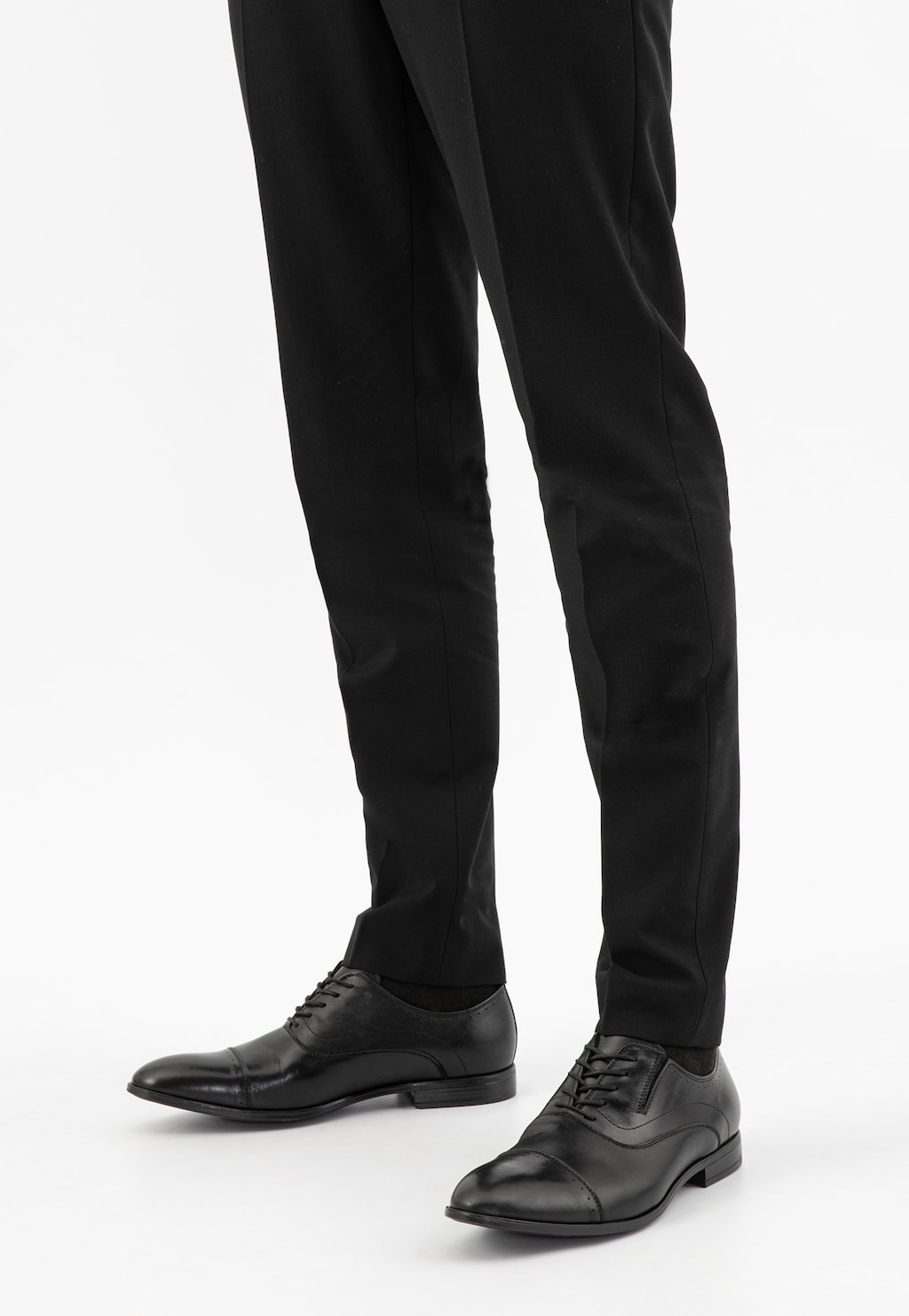 Eleganckie czarne półbuty męskie Wojas model 10165-51 typu quarter brogue widoczne na nogach mężczyzny w czarnych spodniach garniturowych.