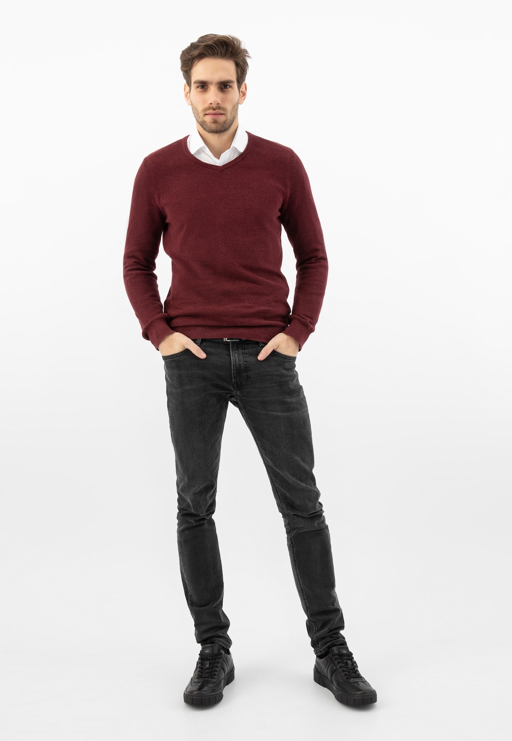 Elegancki model w bordowym swetrze i ciemnych jeansach prezentuje czarne skórzane trampki Wojas 10180-51 ocieplane futerkiem, idealne na chłodniejsze dni.