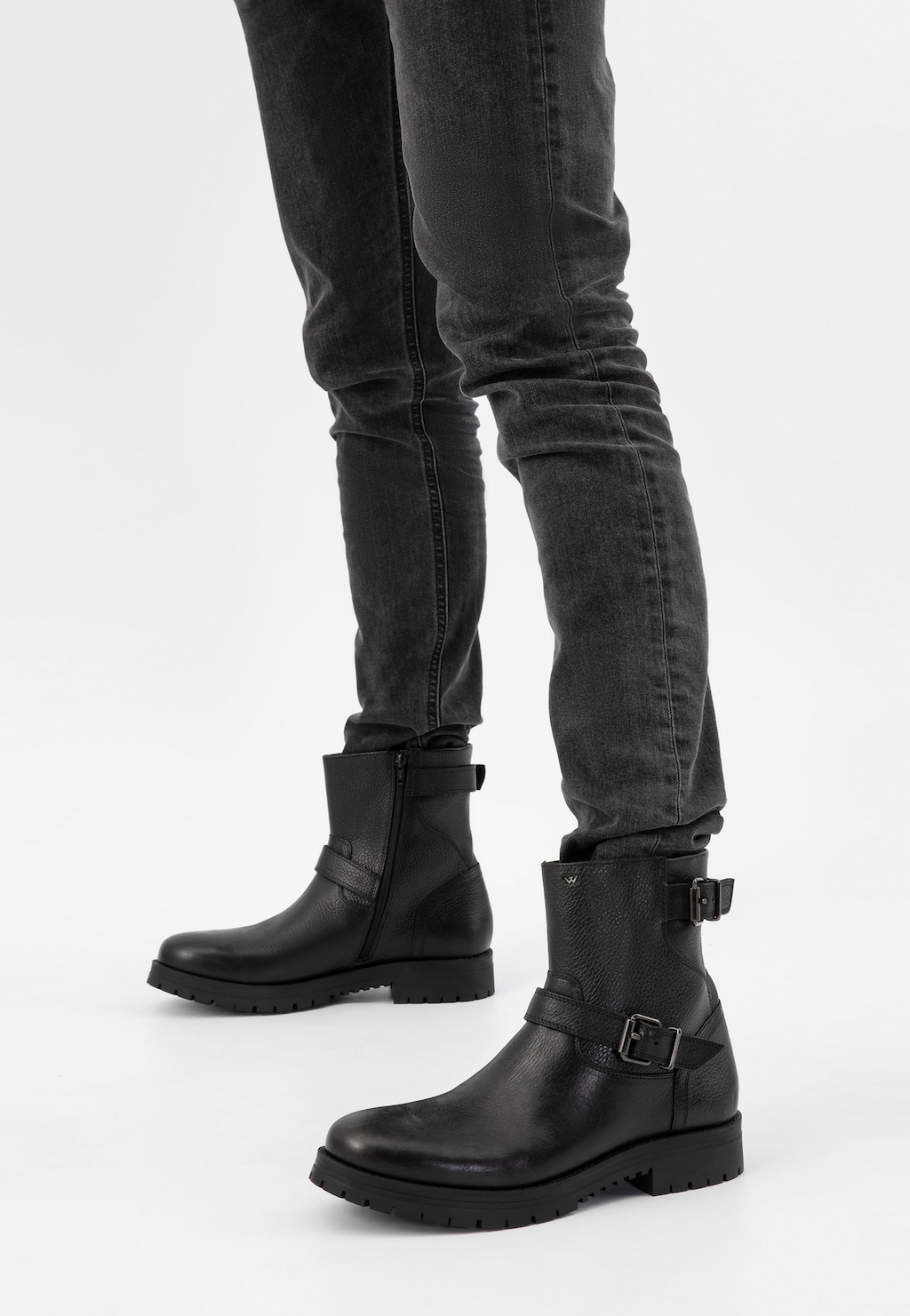 Czarne męskie bikery Wojas 20022-51 ze skóry licowej z klamrami, prezentowane na nogach w ciemnych jeansach. Solidna podeszwa i minimalistyczny design podkreślają rockowy charakter.