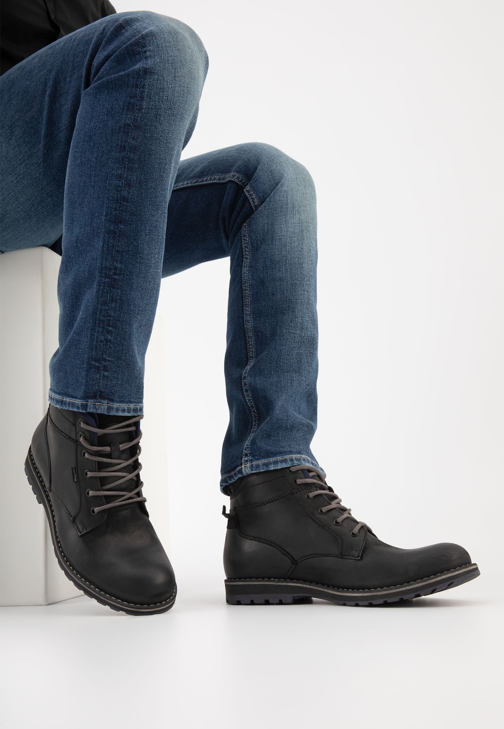 Czarne workery męskie Wojas 24031-71 z granatowymi akcentami prezentowane na nogach modela w niebieskich jeansach. Buty mają sznurowane zapięcie i masywną podeszwę.