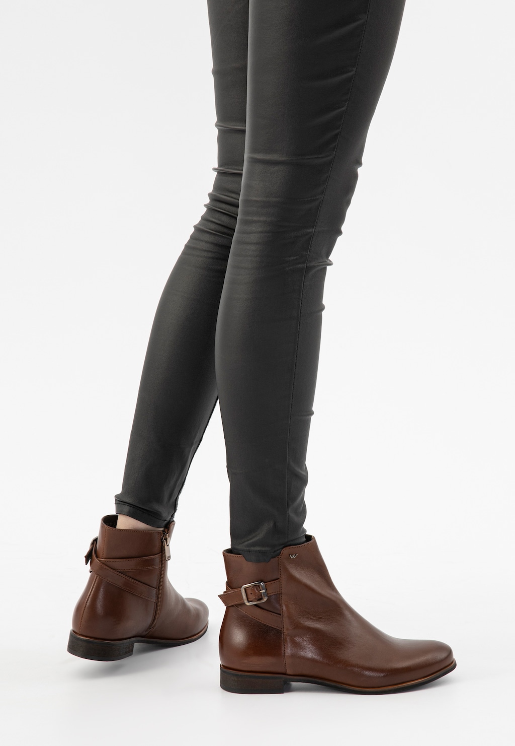 Brązowe jesienne botki damskie Wojas model 55066-50 z zamkiem i dekoracyjnym paskiem z klamrą, zaprezentowane na nogach w czarnych obcisłych spodniach.