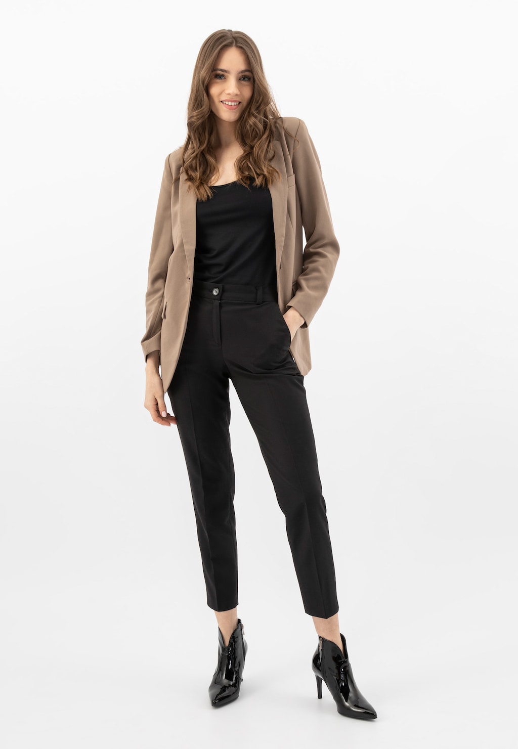 Modelka w eleganckim stroju biznesowym z beżową marynarką i czarnym kombinezonem, prezentująca lakierowane botki na szpilce Wojas model 55096-31.