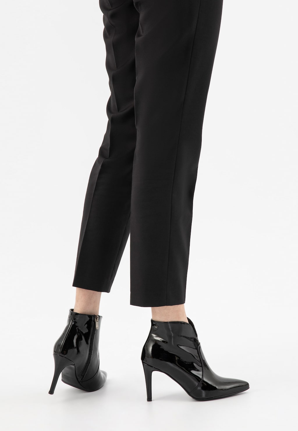 Eleganckie czarne lakierowane botki Wojas model 55096-31 na wysokiej szpilce, prezentowane na nogach modelki w czarnych spodniach, widok z tyłu.
