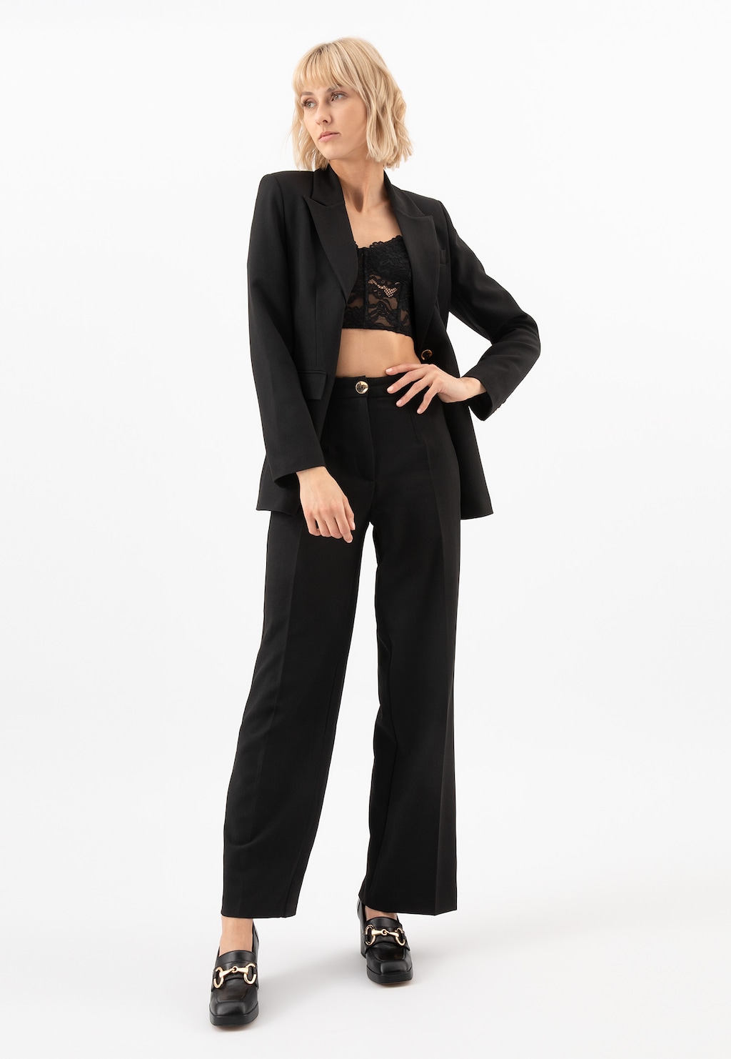 Elegancki czarny garnitur z koronkowym topem, uzupełniony modnymi mokasyniami Wojas 46218-51 - czarnymi skórzanymi butami damskimi na słupku ze złotą ozdobą.