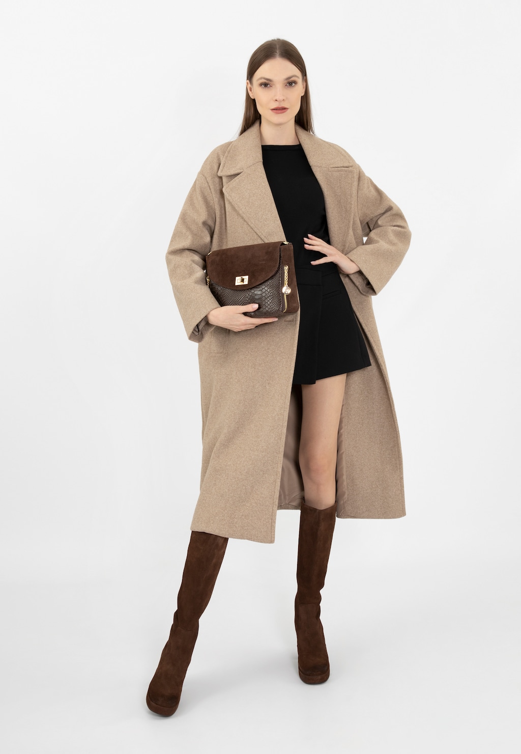 Modelka w beżowym płaszczu i czarnej sukience prezentuje ciemnobrązową torebkę Wojas model 80157-72 z charakterystyczną fakturą, uzupełniając stylizację brązowymi kozakami.