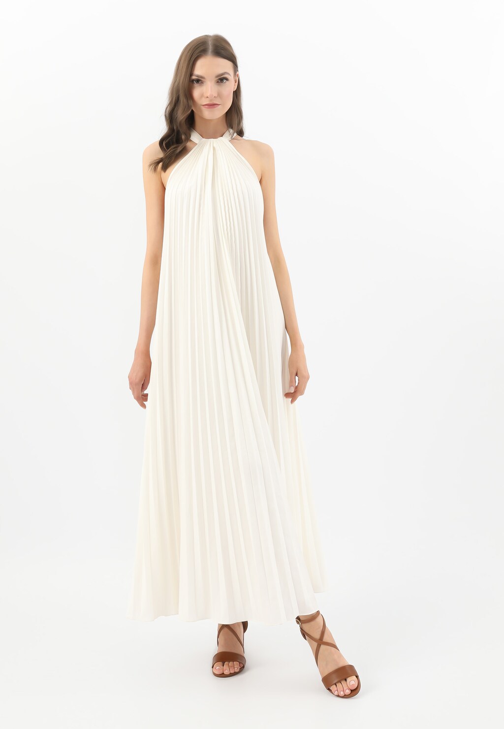Modelka w długiej, plisowanej kreacji w kolorze kremowym, prezentująca sandały Wojas model 76058-53 - skórzane sandały damskie na klocku w jasnobrązowym kolorze.