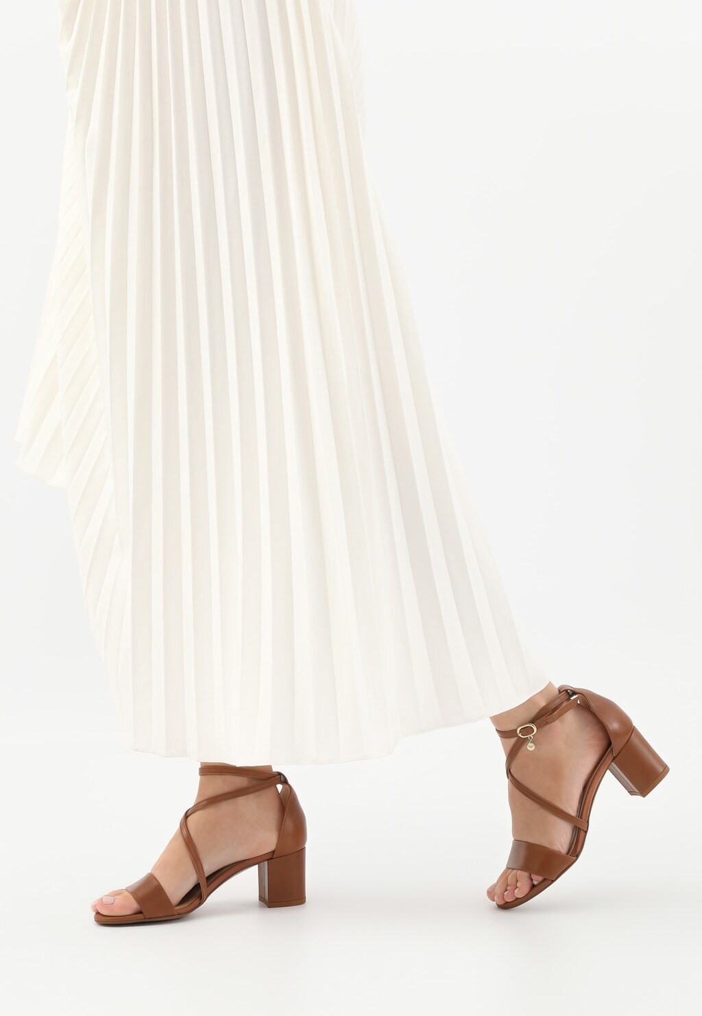 Eleganckie skórzane sandały damskie Wojas 76058-53 w jasnobrązowym kolorze na stabilnym klocku, zapinane na pasek, prezentowane z białą plisowaną spódnicą.