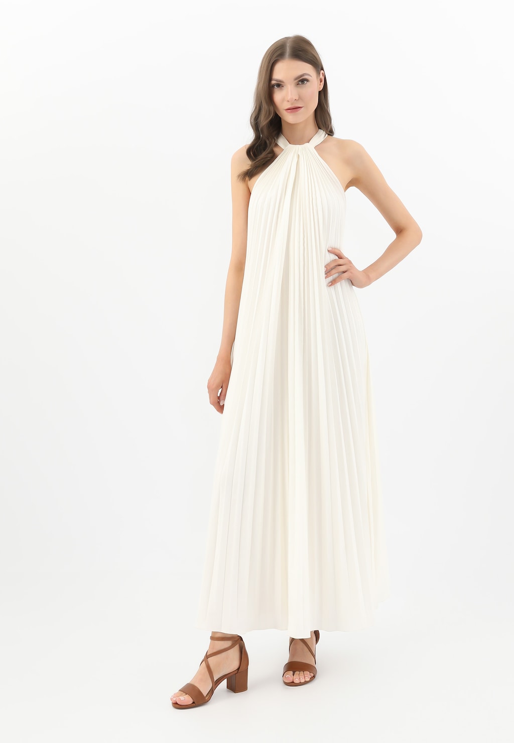 Modelka w białej plisowanej sukni prezentuje skórzane sandały damskie Wojas model 76058-53 na klocku w jasnobrązowym kolorze, z krzyżowymi paskami.