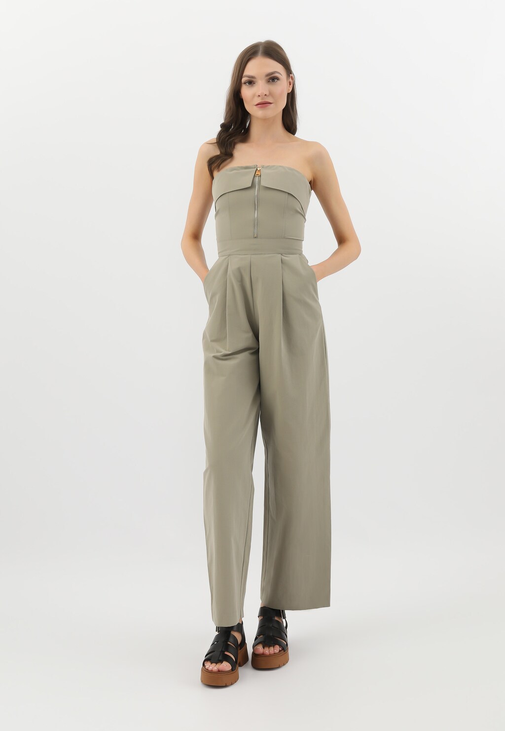 Modelka w beżowym kombinezonie z odkrytymi ramionami, prezentująca czarne sandały damskie Wojas model 76136-51 z szerokimi paskami na platformie w kolorze brązowym.