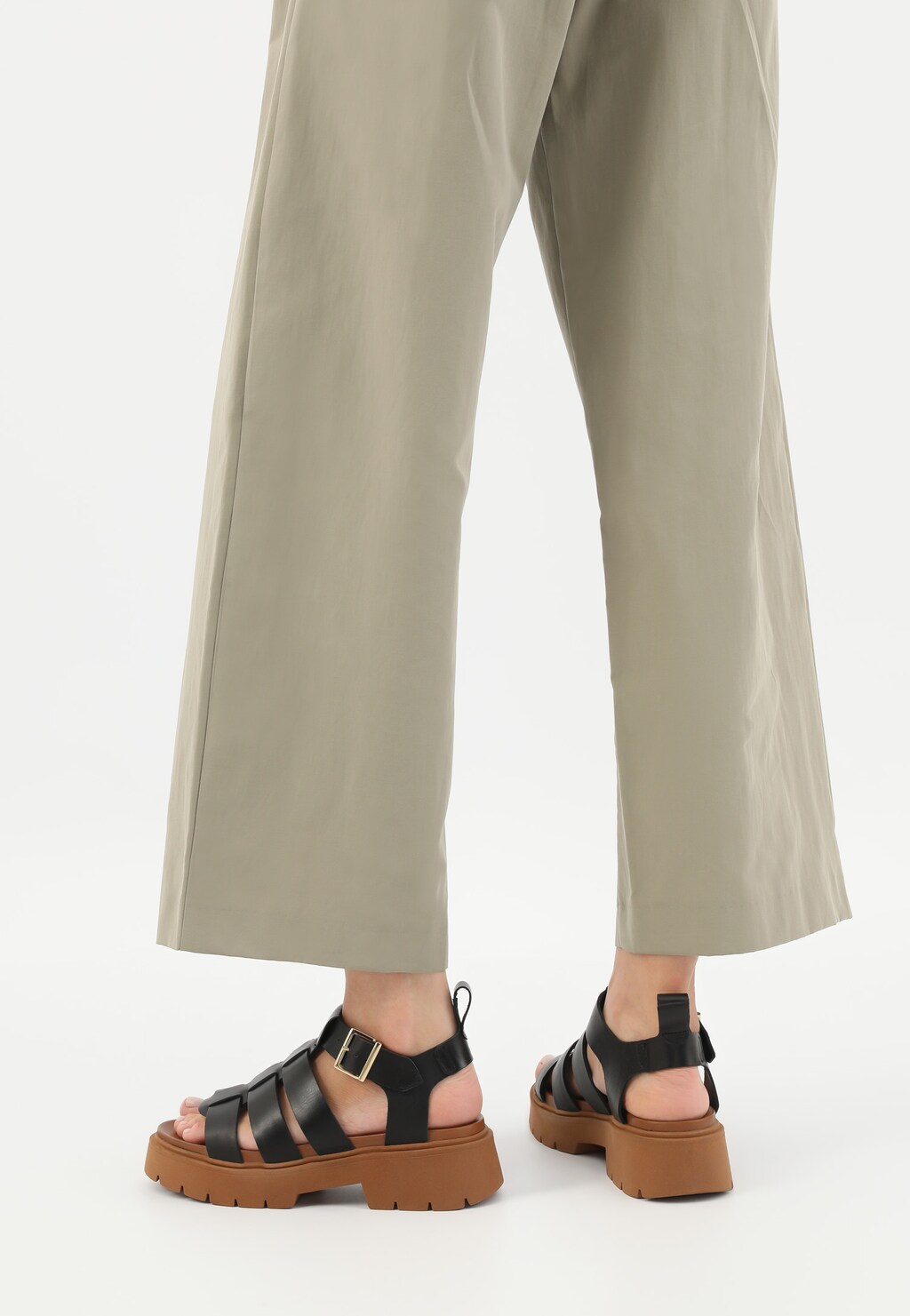 Czarne sandały damskie Wojas model 76136-51 z szerokimi paskami na masywnej brązowej podeszwie, noszone do beżowych szerokich spodni.