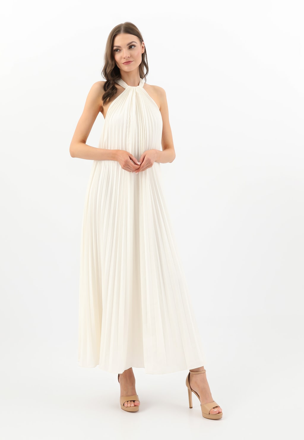 Modelka w długiej białej sukni plisowanej z wiązaniem przy szyi, prezentująca wysokie beżowe sandały na szpilce Wojas model 76152-50.
