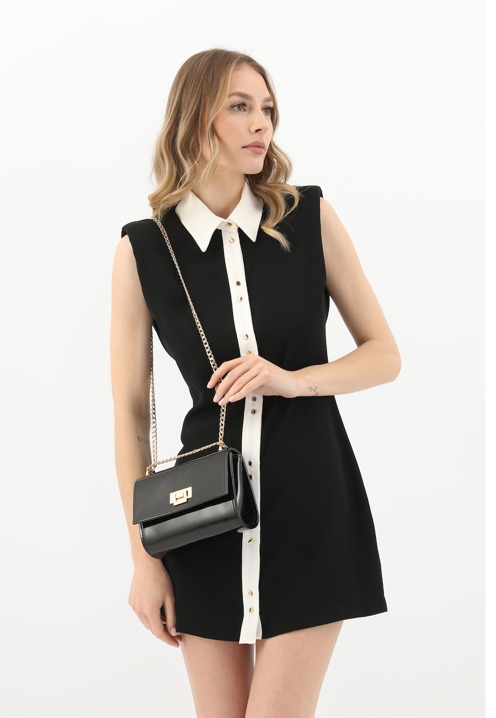 Elegancka czarna lakierowana torebka Wojas 80374-31 ze złotym łańcuchem prezentowana na modelce w czarnej sukience z białym kołnierzykiem.