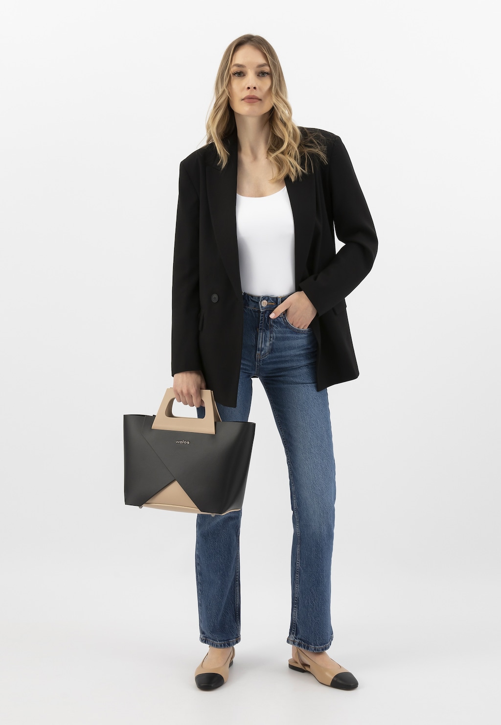 Elegancka stylizacja z dwukolorowymi balerinami Wojas model 44032-54. Kobieta w czarnym żakiecie, białym topie i jeansach, trzymająca dwukolorową torebkę.