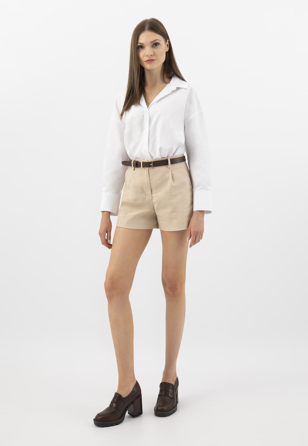 Modelka w eleganckim stroju z białą koszulą i beżowymi szortami, prezentująca brązowe mokasyny damskie Wojas model 46239-52 ze skóry licowej na słupku.