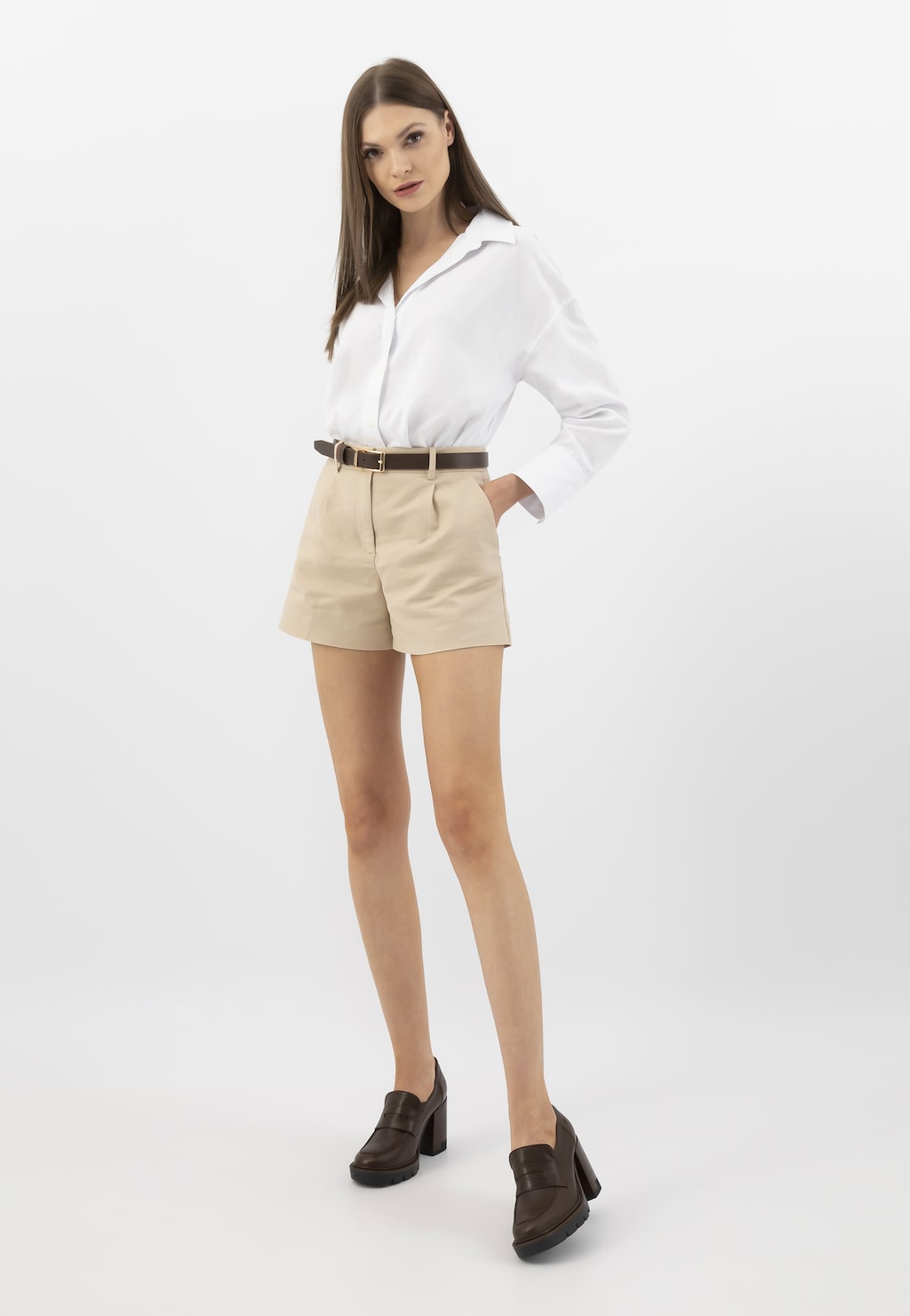 Modelka w eleganckim stroju z białą koszulą i beżowymi szortami, prezentująca brązowe mokasyny damskie Wojas model 46239-52 ze skóry licowej na słupku.