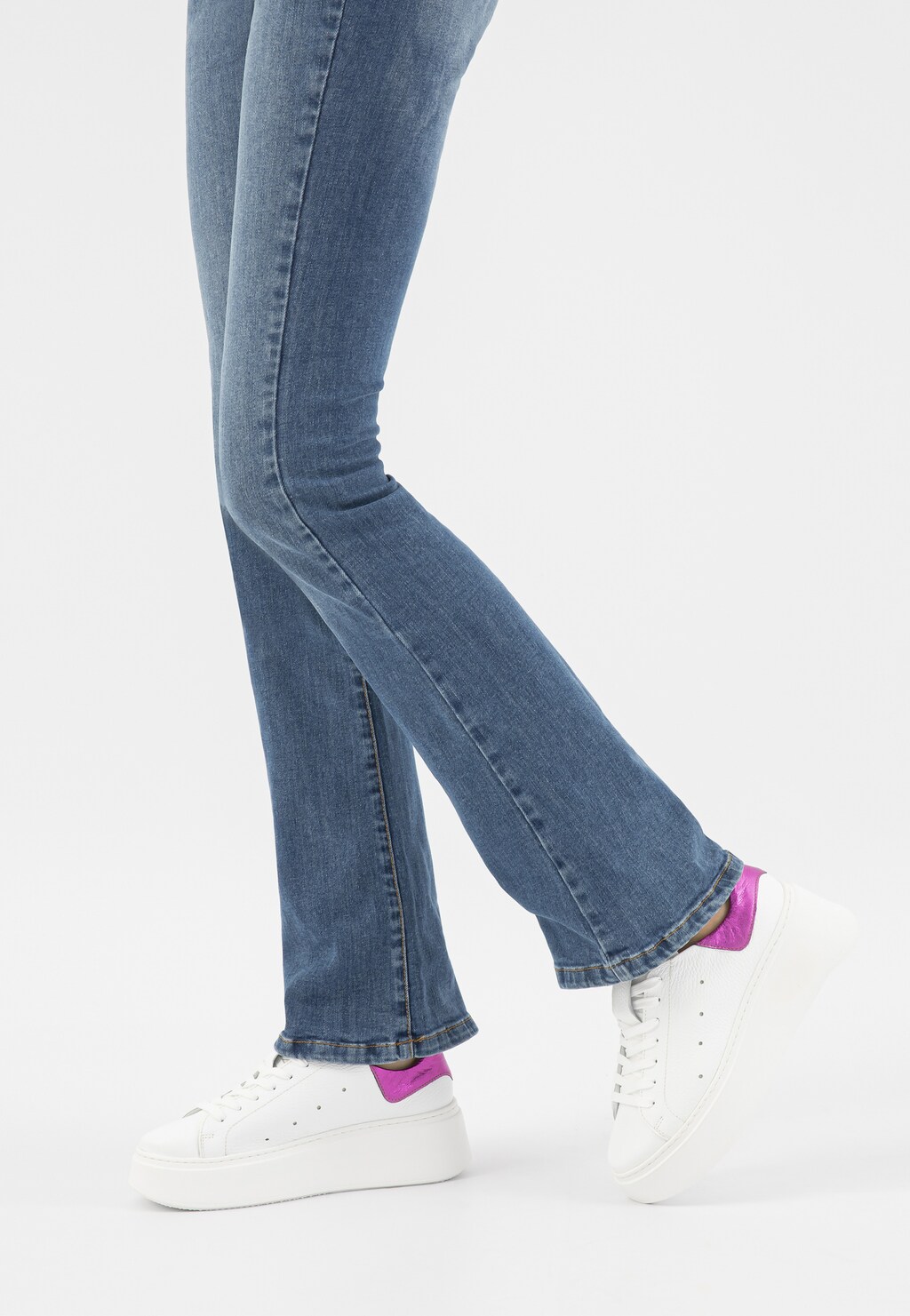 Białe trampki Wojas model 46285-75 z różową metaliczną wstawką noszone z jeansami. Widok pokazuje buty na nogach w ujęciu bocznym.
